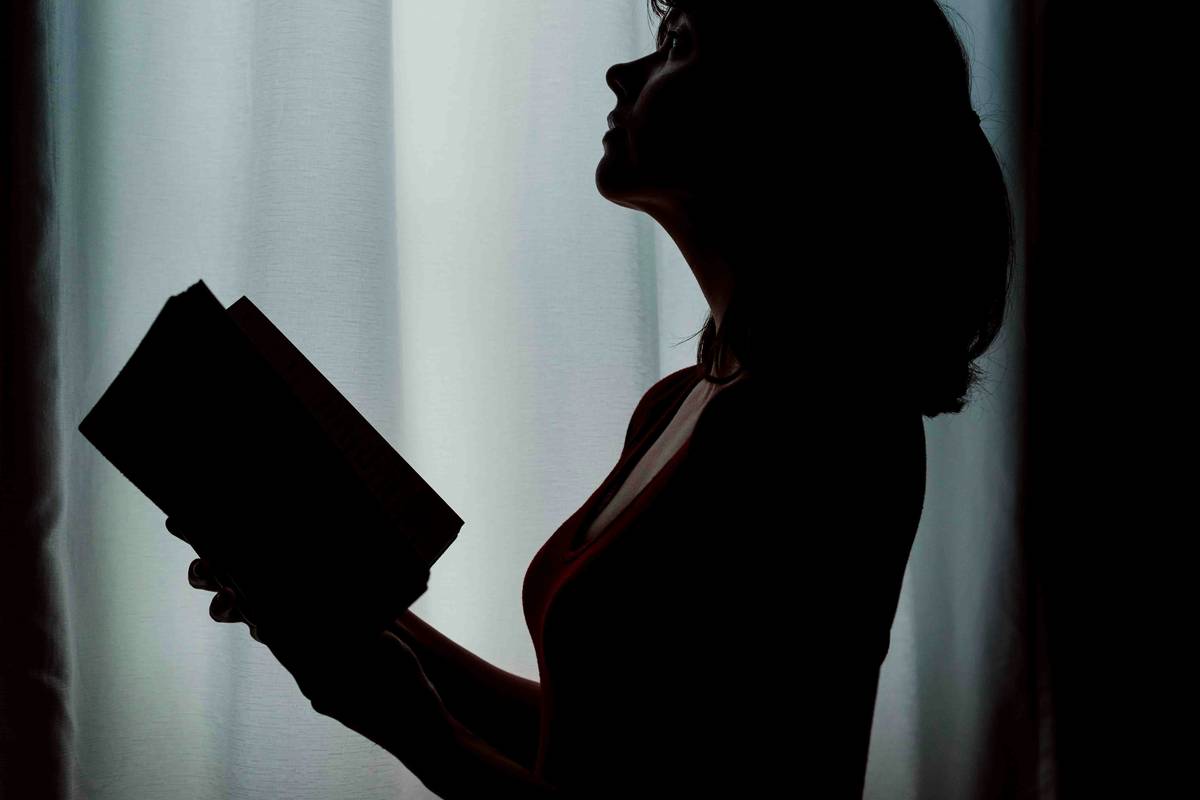 Stack of great psychological thriller books on a dimly lit desk beside a vintage lamp